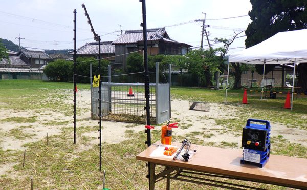 屋外設置の電気柵（手前）と捕獲檻（奥）の様子